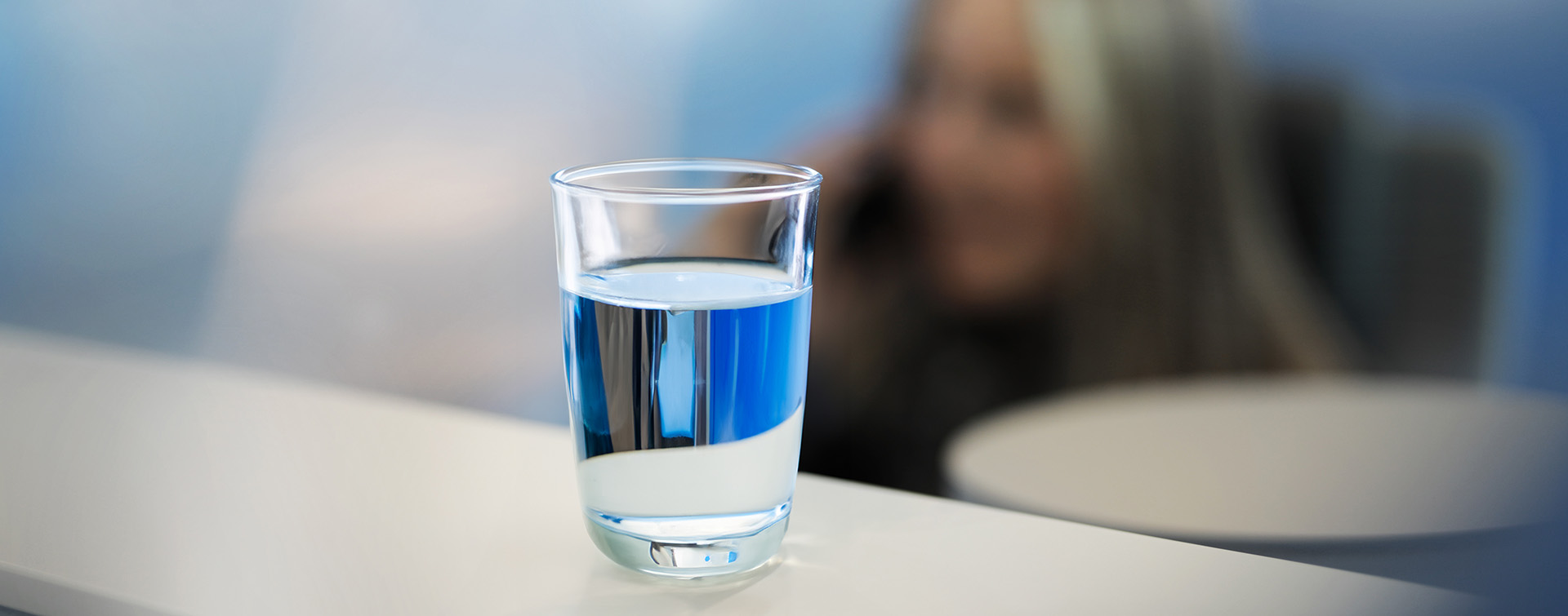 Wasserglas als Symbol für Liquidität mit telefonierender Frau im Hintergrund.