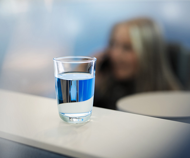 Wasserglas mit telefonierender Frau im Hintergrund