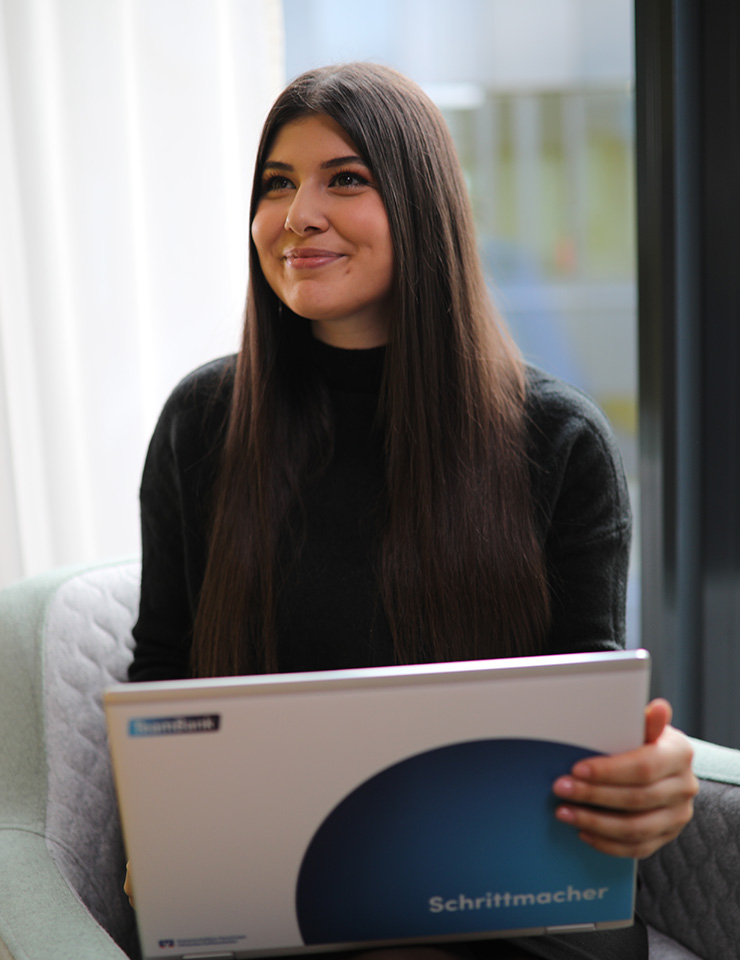 Junge Mitarbeiterin sitzt freudig mit TeamBank Laptop in Sessel.