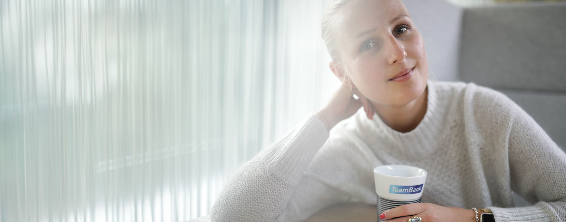 Unbeschwerte Frau mit TeamBank-Becher lehnt auf ihrem Arm.